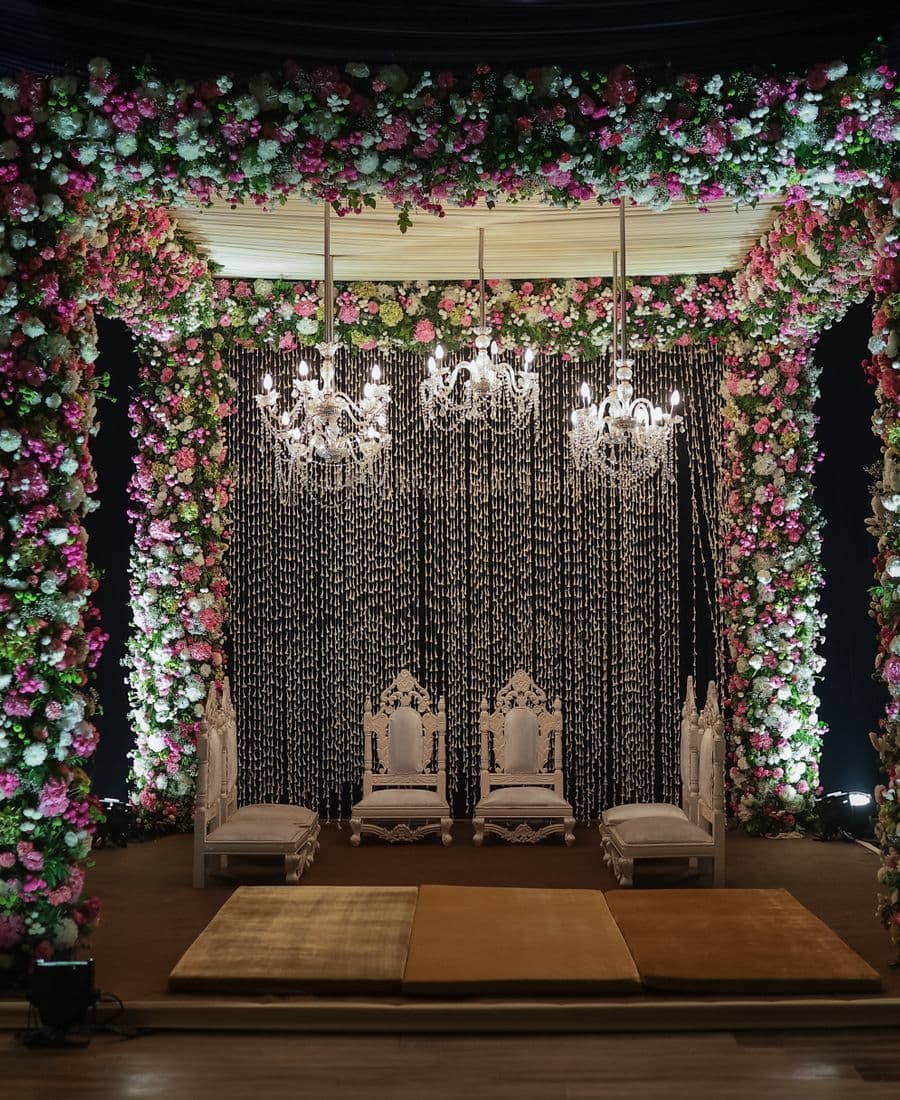 A flower-decorated wedding mandap with chandeliers and carved seating